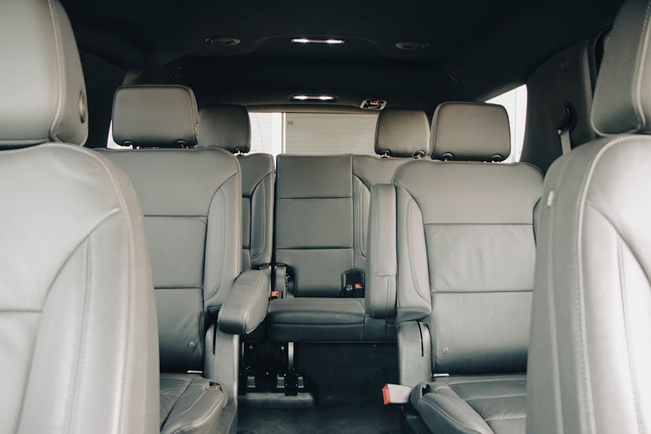 Photograph of the interior of a vehicle showing three rows of grey leather seats, which are clean and well-maintained. The seats have visible stitching and headrests, with some seats folded down to indicate flexible seating arrangements. The vehicle's black ceiling and side panels are visible, with subtle lighting and window reflections. The flooring appears to be dark and free of debris, and some visible seat belts are neatly positioned. Overall, the interior demonstrates a high standard of cleanliness, reflecting professional upholstery deep cleaning, as provided by Carpet Cleaners Highbury, on Holloway Road, HIGHBURY.