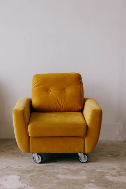 A person wearing black gloves is using a yellow handheld upholstery cleaning machine on a dark grey fabric sofa in a living room. The sofa has a modern design with clean lines and is positioned against a white wall. The cleaning process appears to be part of deep cleaning or surface sanitisation, with a focus on removing dirt and stains from the upholstery fabric. To the right of the sofa, there is a decorated Christmas tree with ornaments, indicating a festive setting. The room has wooden flooring, and natural light illuminates the scene, emphasizing the clean and maintained condition of the furniture. Carpet Cleaners Highbury offers professional domestic cleaning services, including upholstery cleaning, to ensure hygiene and freshness in residential spaces.