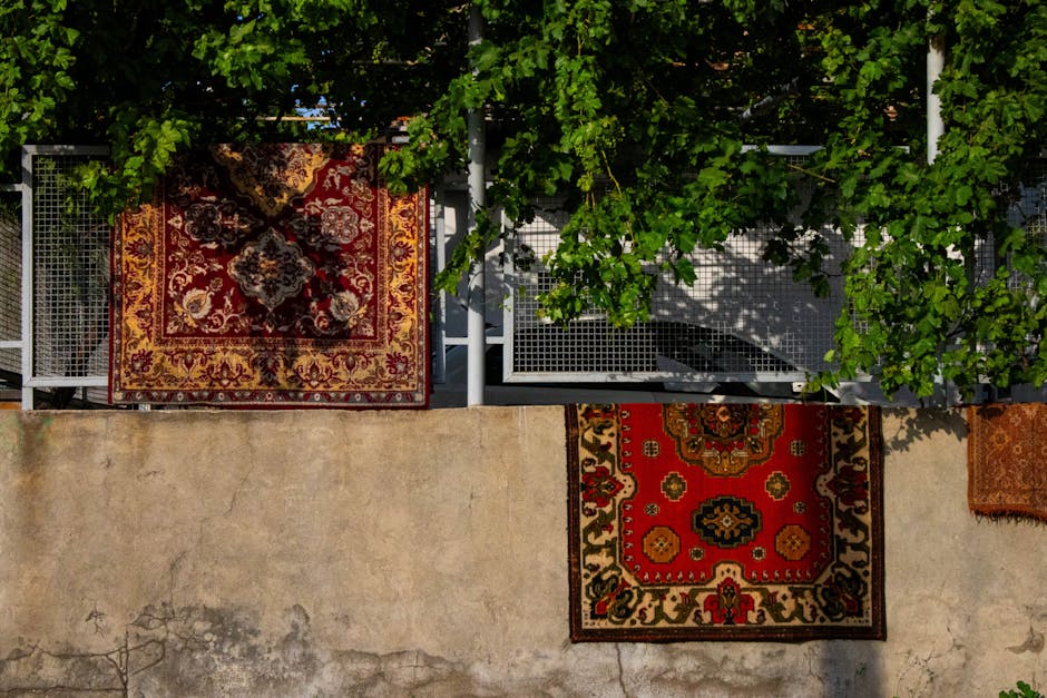 Close-up view of two patterned area rugs placed on a white, textured concrete floor. The rug on the left features a traditional design with red, navy, white, and light blue geometric motifs, while the